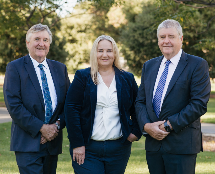 Group photo outdoors of Simon, Deidre and Guy. They are standing together in navy blue and white corporate attire with relaxed and approachable smiles.